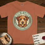 Dog is Love T-Shirt flat lay in Yam, featuring a vintage distressed circular badge with a scruffy terrier on a sage-green ground, the words Dog Is Love and Unconditional Forever, and flanking paw prints.