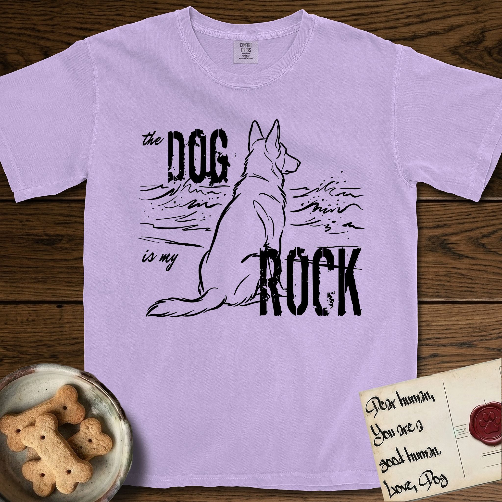 DIMR German Shepherd T-Shirt flat lay in Orchid, featuring ink-line illustration of a German Shepherd seen from behind, sitting at the waterline and watching a stormy sea, with the words the Dog is my Rock.