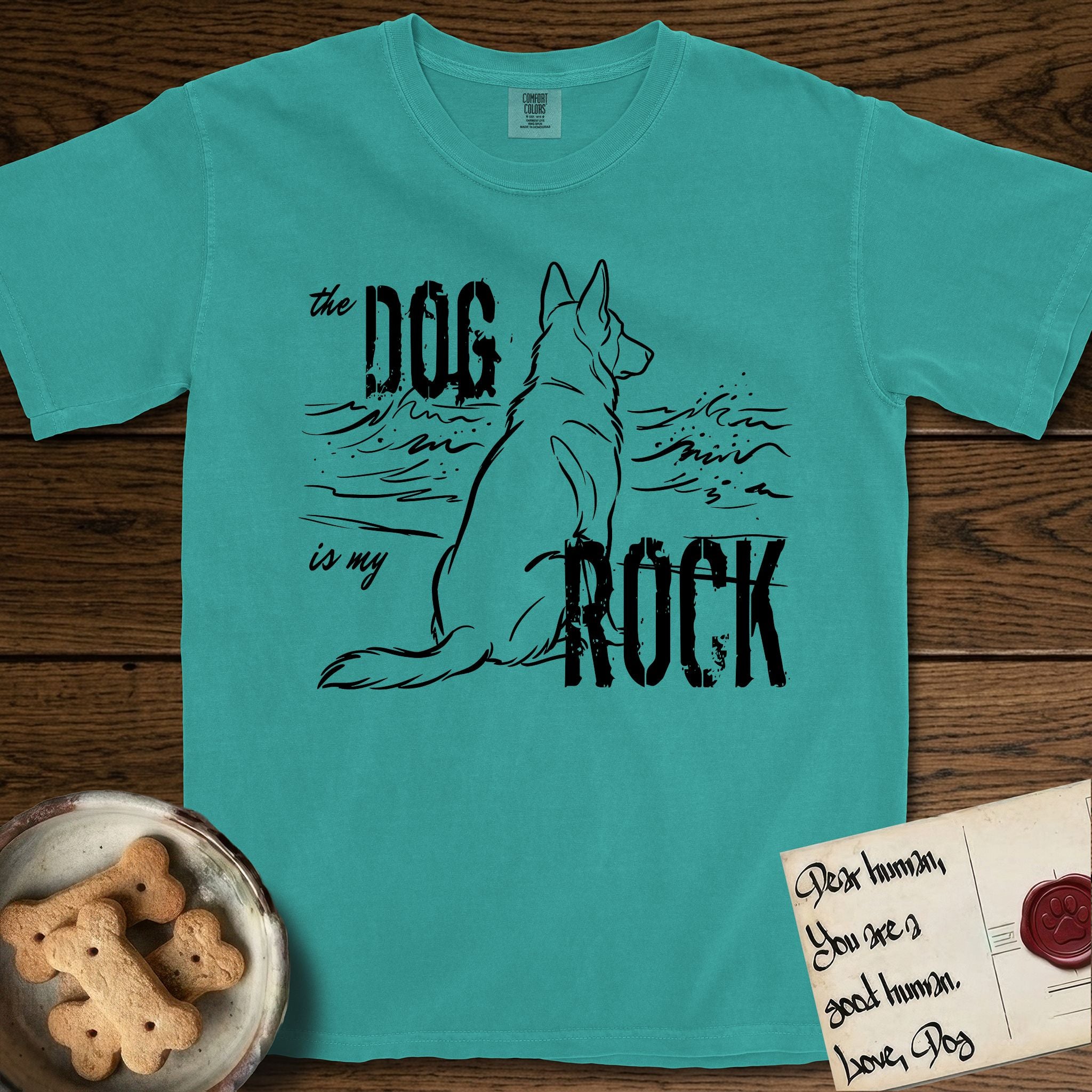 DIMR German Shepherd T-Shirt flat lay in Seafoam, featuring ink-line illustration of a German Shepherd seen from behind, sitting at the waterline and watching a stormy sea, with the words the Dog is my Rock.