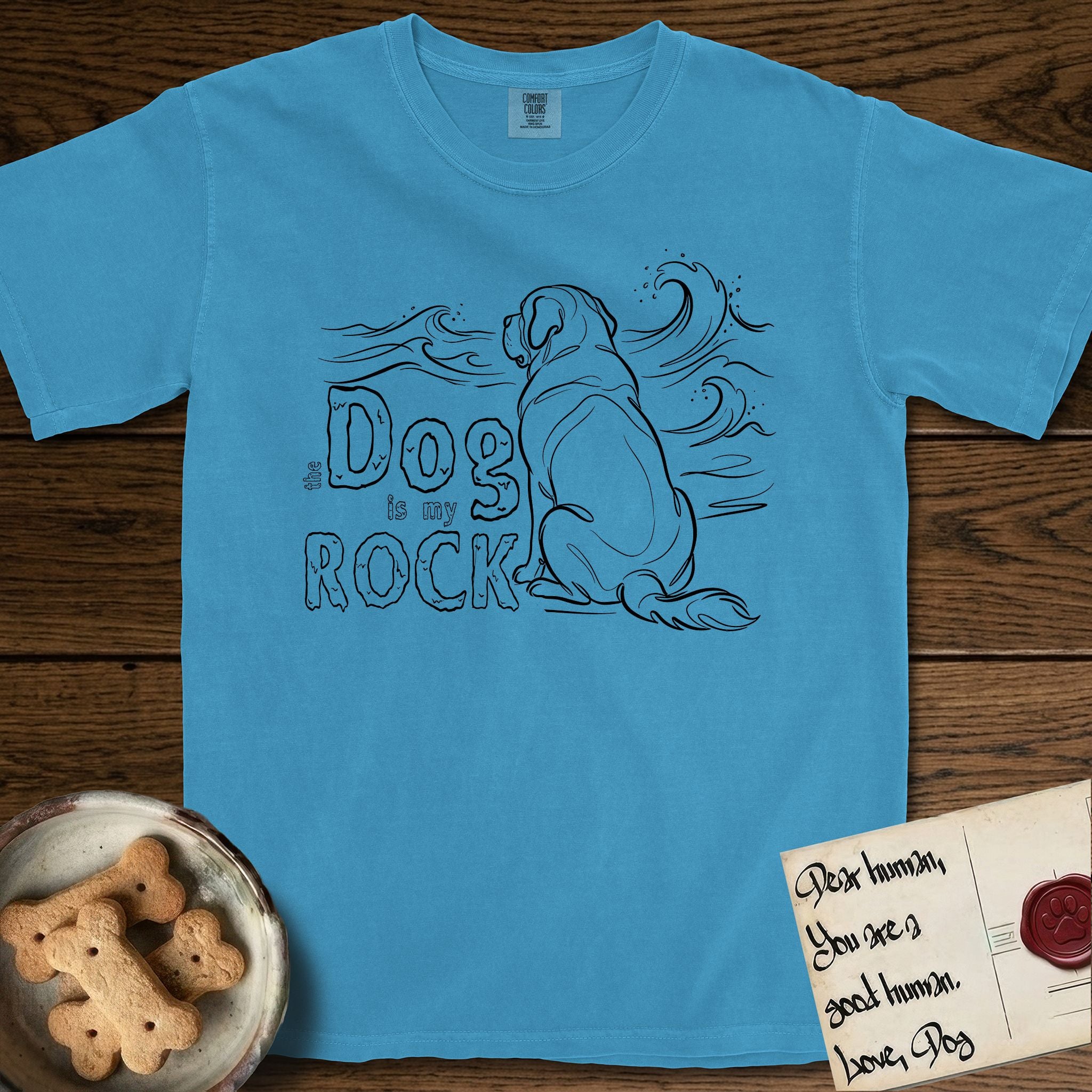 DIMR Saint Bernard T-Shirt flat lay in Royal Caribe, featuring ink-line illustration of a Saint Bernard seen from behind, sitting at the water's edge and watching a stormy sea, with the words the Dog is my Rock.