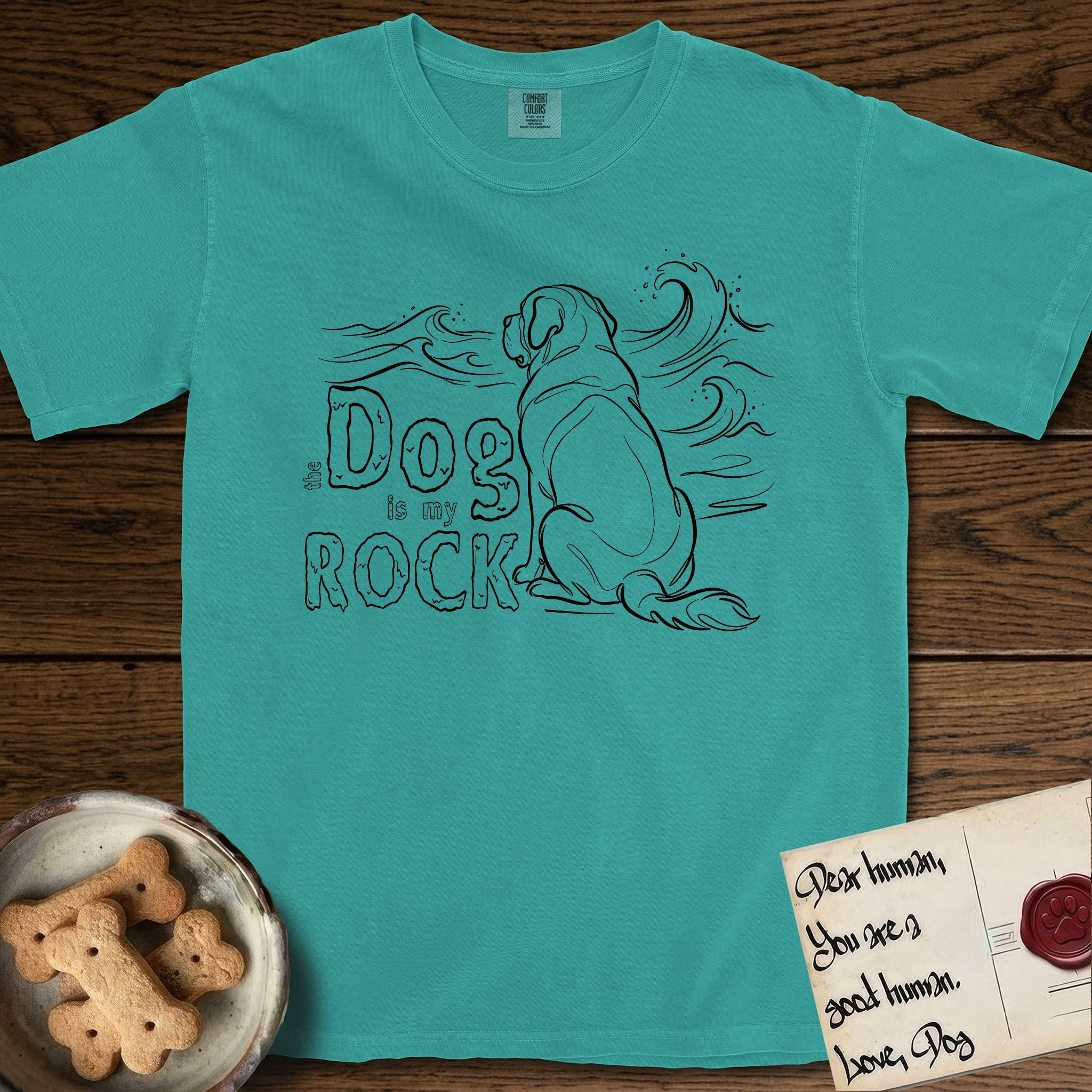 DIMR Saint Bernard T-Shirt flat lay in Seafoam, featuring ink-line illustration of a Saint Bernard seen from behind, sitting at the water's edge and watching a stormy sea, with the words the Dog is my Rock.