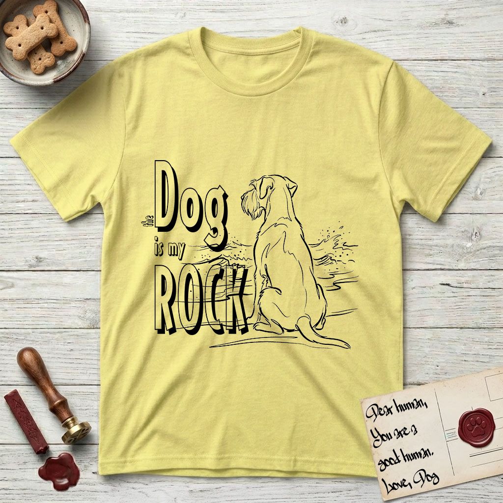 DIMR Schnauzer T-Shirt flat lay in Cornsilk, featuring ink-line illustration of a Schnauzer seen from behind at the water's edge, head turned toward a stormy sea, with the words the Dog is my Rock.