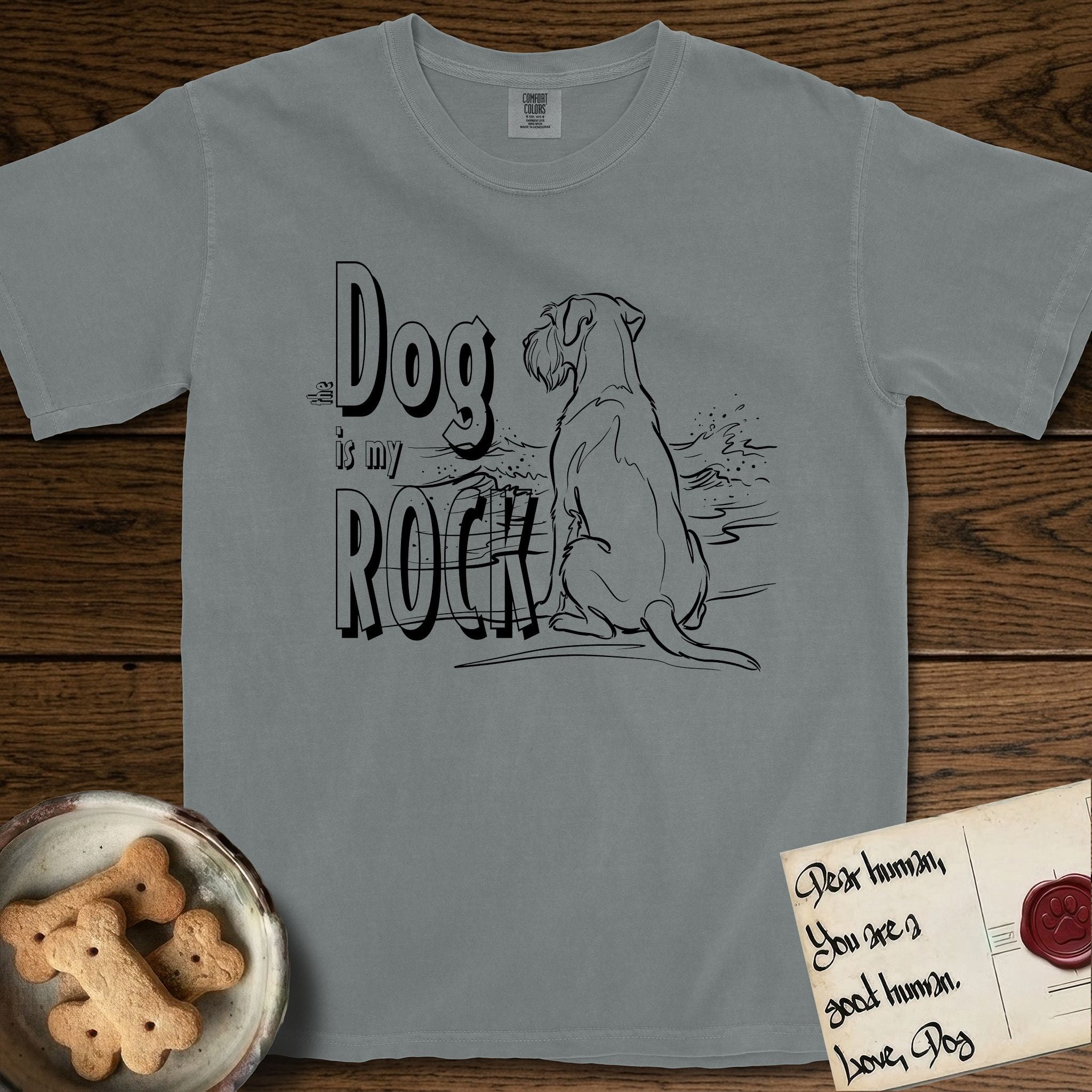 DIMR Schnauzer T-Shirt flat lay in Granite, featuring ink-line illustration of a Schnauzer seen from behind at the water's edge, head turned toward a stormy sea, with the words the Dog is my Rock.