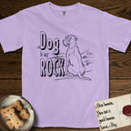 DIMR Schnauzer T-Shirt flat lay in Orchid, featuring ink-line illustration of a Schnauzer seen from behind at the water's edge, head turned toward a stormy sea, with the words the Dog is my Rock.