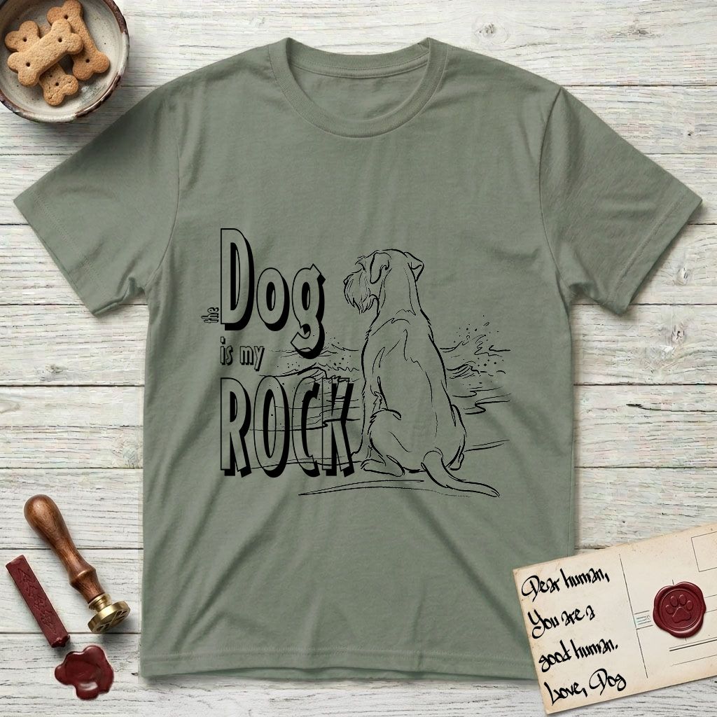 DIMR Schnauzer T-Shirt flat lay in Sage, featuring ink-line illustration of a Schnauzer seen from behind at the water's edge, head turned toward a stormy sea, with the words the Dog is my Rock.
