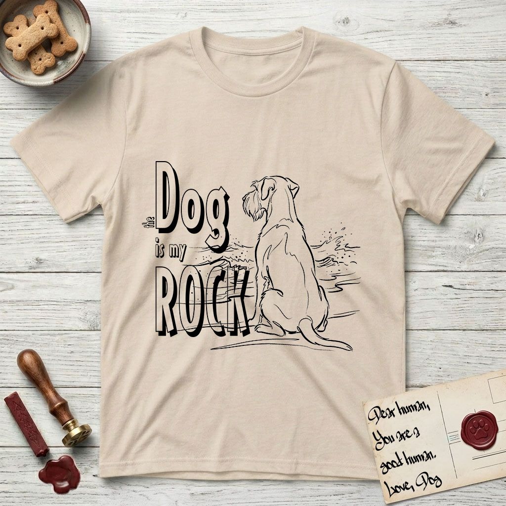 DIMR Schnauzer T-Shirt flat lay in Sand, featuring ink-line illustration of a Schnauzer seen from behind at the water's edge, head turned toward a stormy sea, with the words the Dog is my Rock.