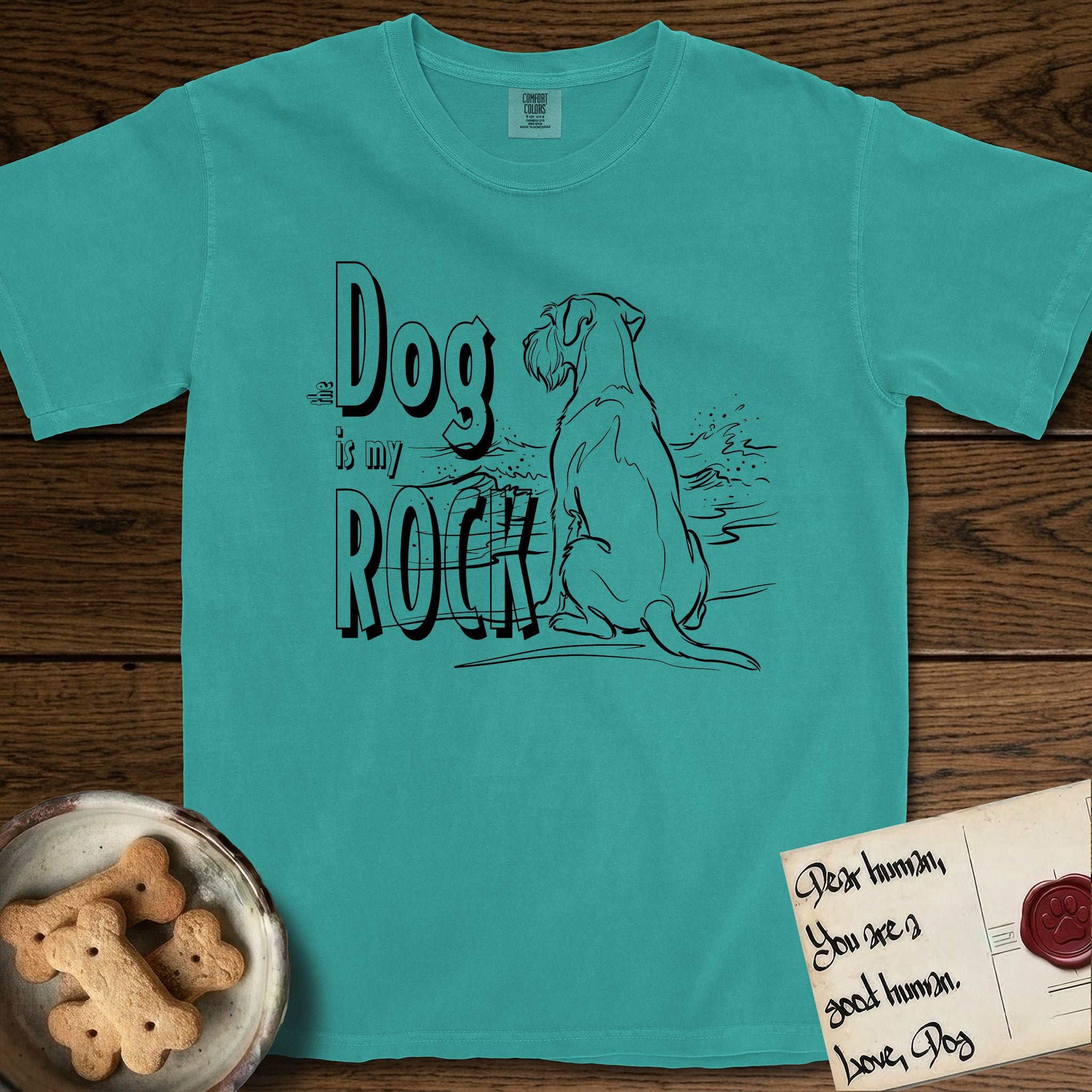 DIMR Schnauzer T-Shirt flat lay in Seafoam, featuring ink-line illustration of a Schnauzer seen from behind at the water's edge, head turned toward a stormy sea, with the words the Dog is my Rock.
