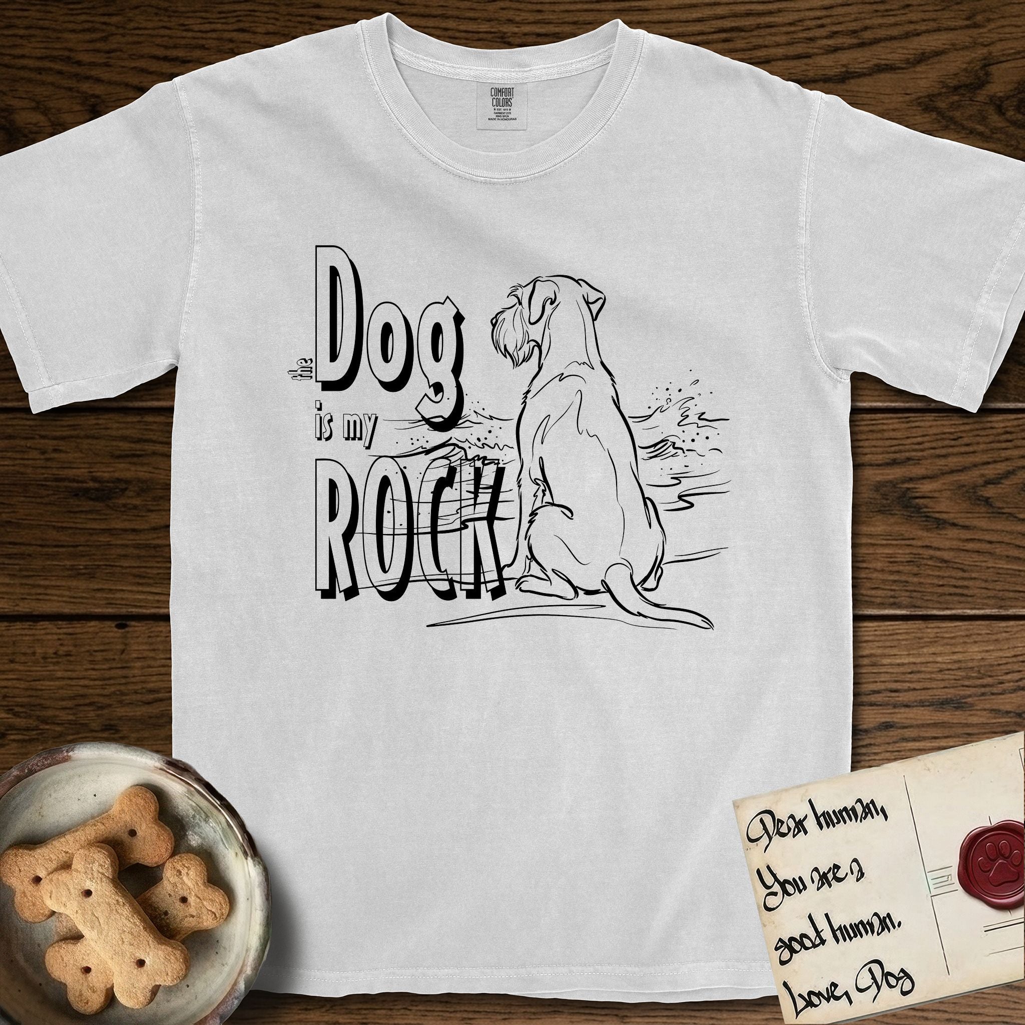 DIMR Schnauzer T-Shirt flat lay in White, featuring ink-line illustration of a Schnauzer seen from behind at the water's edge, head turned toward a stormy sea, with the words the Dog is my Rock.