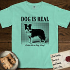 Dog is Real Border Collie T-Shirt flat lay in Island Reef, featuring Black halftone newspaper photo of a black and white Border Collie standing in profile with head turned to the camera, under the headline DOG IS REAL, with the caption Praise Be to Dog. Woof..