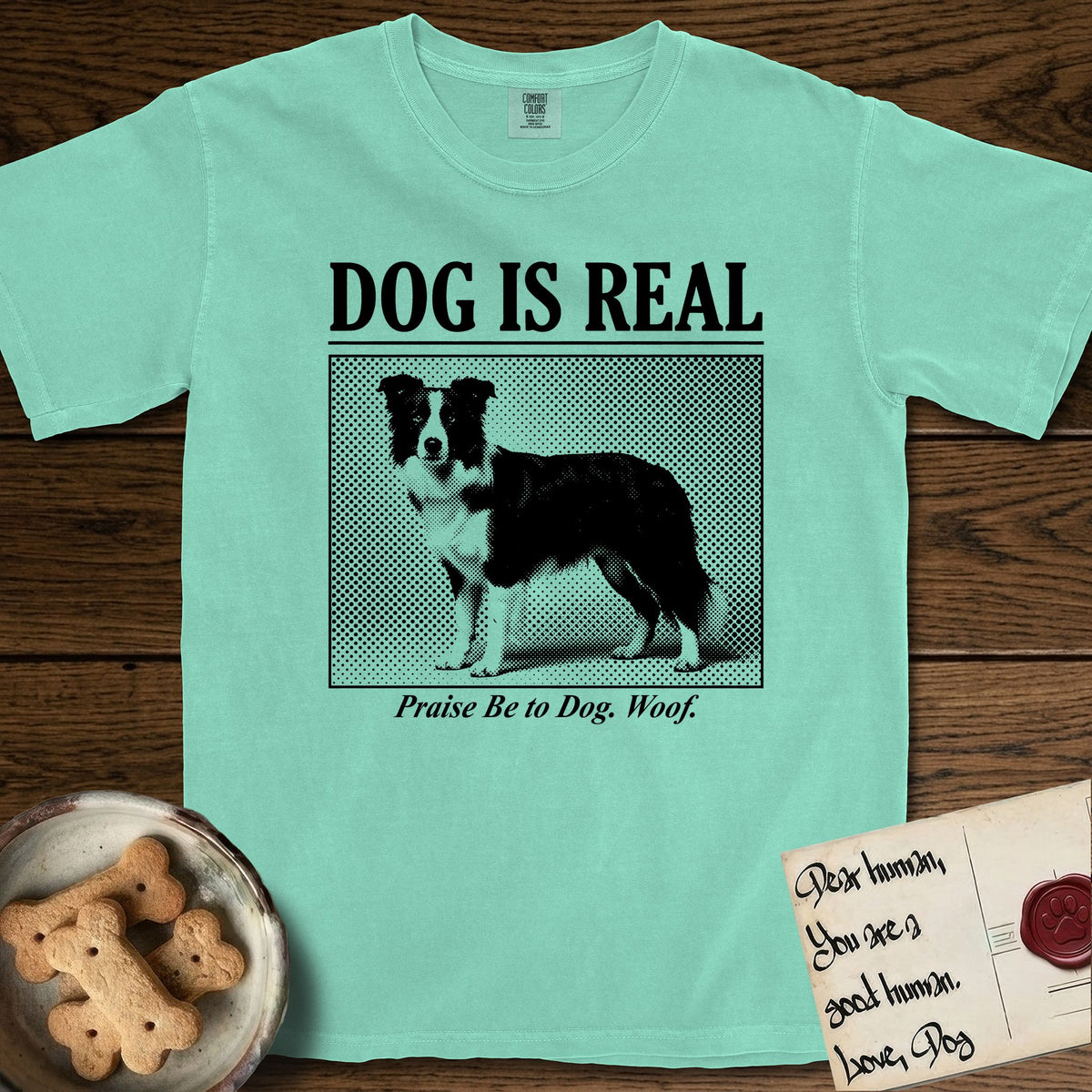 Dog is Real Border Collie T-Shirt flat lay in Island Reef, featuring Black halftone newspaper photo of a black and white Border Collie standing in profile with head turned to the camera, under the headline DOG IS REAL, with the caption Praise Be to Dog. Woof..