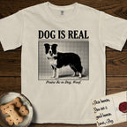 Dog is Real Border Collie T-Shirt flat lay in Ivory, featuring Black halftone newspaper photo of a black and white Border Collie standing in profile with head turned to the camera, under the headline DOG IS REAL, with the caption Praise Be to Dog. Woof..