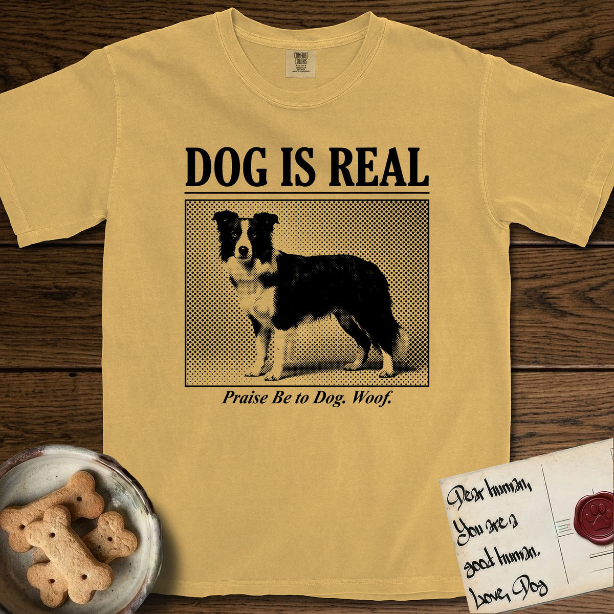 Dog is Real Border Collie T-Shirt flat lay in Mustard, featuring Black halftone newspaper photo of a black and white Border Collie standing in profile with head turned to the camera, under the headline DOG IS REAL, with the caption Praise Be to Dog. Woof..