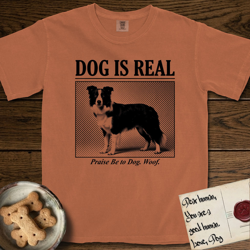 Dog is Real Border Collie T-Shirt flat lay in Yam, featuring Black halftone newspaper photo of a black and white Border Collie standing in profile with head turned to the camera, under the headline DOG IS REAL, with the caption Praise Be to Dog. Woof..