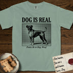 Dog is Real Boxer T-Shirt flat lay in Bay, featuring Black halftone newspaper photo of a Boxer with a white chest standing in profile with head turned to the camera, under the headline DOG IS REAL, with the caption Praise Be to Dog. Woof..