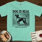 Dog is Real Boxer T-Shirt flat lay in Island Reef, featuring Black halftone newspaper photo of a Boxer with a white chest standing in profile with head turned to the camera, under the headline DOG IS REAL, with the caption Praise Be to Dog. Woof..