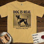 Dog is Real Boxer T-Shirt flat lay in Mustard, featuring Black halftone newspaper photo of a Boxer with a white chest standing in profile with head turned to the camera, under the headline DOG IS REAL, with the caption Praise Be to Dog. Woof..