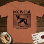 Dog is Real Boxer T-Shirt flat lay in Yam, featuring Black halftone newspaper photo of a Boxer with a white chest standing in profile with head turned to the camera, under the headline DOG IS REAL, with the caption Praise Be to Dog. Woof..