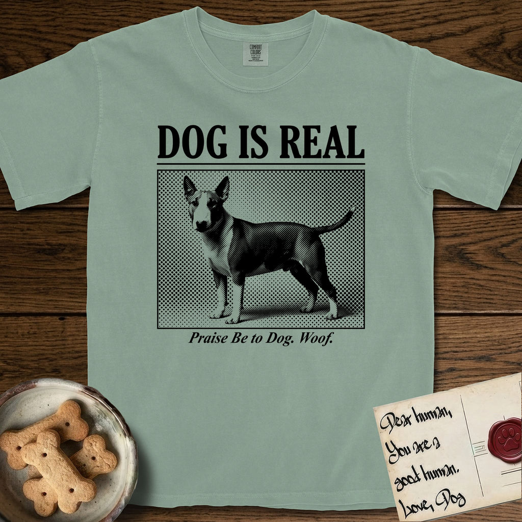 Dog is Real Bull Terrier T-Shirt flat lay in Bay, featuring Black halftone newspaper photo of a Bull Terrier with a white face standing in profile with head turned to the camera, under the headline DOG IS REAL, with the caption Praise Be to Dog. Woof..