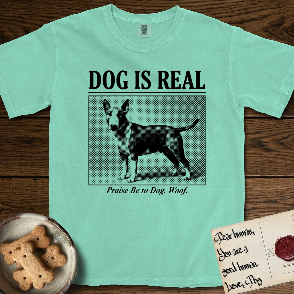 Dog is Real Bull Terrier T-Shirt flat lay in Island Reef, featuring Black halftone newspaper photo of a Bull Terrier with a white face standing in profile with head turned to the camera, under the headline DOG IS REAL, with the caption Praise Be to Dog. Woof..