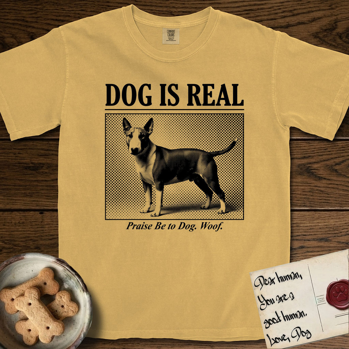 Dog is Real Bull Terrier T-Shirt flat lay in Mustard, featuring Black halftone newspaper photo of a Bull Terrier with a white face standing in profile with head turned to the camera, under the headline DOG IS REAL, with the caption Praise Be to Dog. Woof..