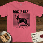 Dog is Real Bull Terrier T-Shirt flat lay in Watermelon, featuring Black halftone newspaper photo of a Bull Terrier with a white face standing in profile with head turned to the camera, under the headline DOG IS REAL, with the caption Praise Be to Dog. Woof..