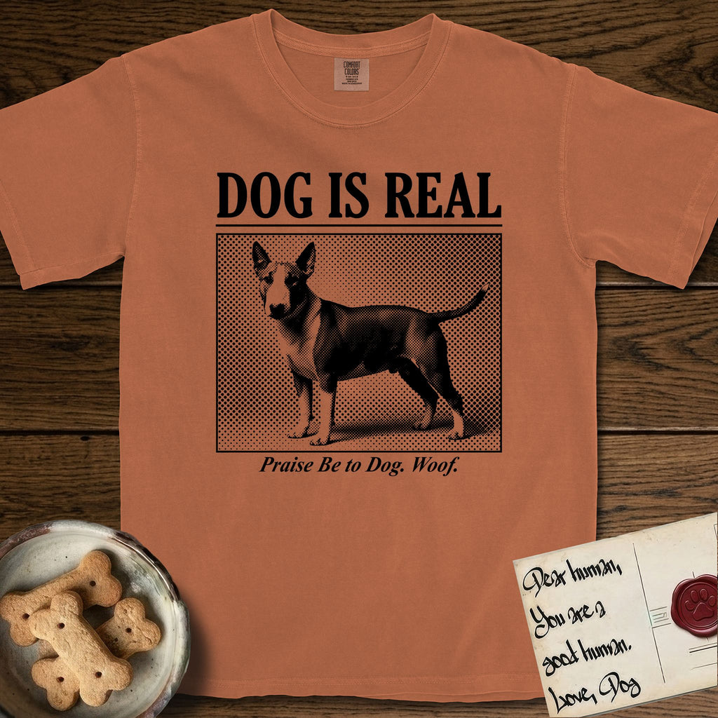 Dog is Real Bull Terrier T-Shirt flat lay in Yam, featuring Black halftone newspaper photo of a Bull Terrier with a white face standing in profile with head turned to the camera, under the headline DOG IS REAL, with the caption Praise Be to Dog. Woof..