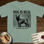 Dog is Real Cairn Terrier T-Shirt flat lay in Bay, featuring Black halftone newspaper photo of a shaggy Cairn Terrier with upright ears and tail standing in profile with head turned to the camera, under the headline DOG IS REAL, with the caption Praise Be to Dog. Woof..
