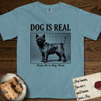 Dog is Real Cairn Terrier T-Shirt flat lay in Ice Blue, featuring Black halftone newspaper photo of a shaggy Cairn Terrier with upright ears and tail standing in profile with head turned to the camera, under the headline DOG IS REAL, with the caption Praise Be to Dog. Woof..