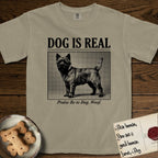 Dog is Real Cairn Terrier T-Shirt flat lay in Khaki, featuring Black halftone newspaper photo of a shaggy Cairn Terrier with upright ears and tail standing in profile with head turned to the camera, under the headline DOG IS REAL, with the caption Praise Be to Dog. Woof..