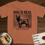 Dog is Real Cairn Terrier T-Shirt flat lay in Yam, featuring Black halftone newspaper photo of a shaggy Cairn Terrier with upright ears and tail standing in profile with head turned to the camera, under the headline DOG IS REAL, with the caption Praise Be to Dog. Woof..