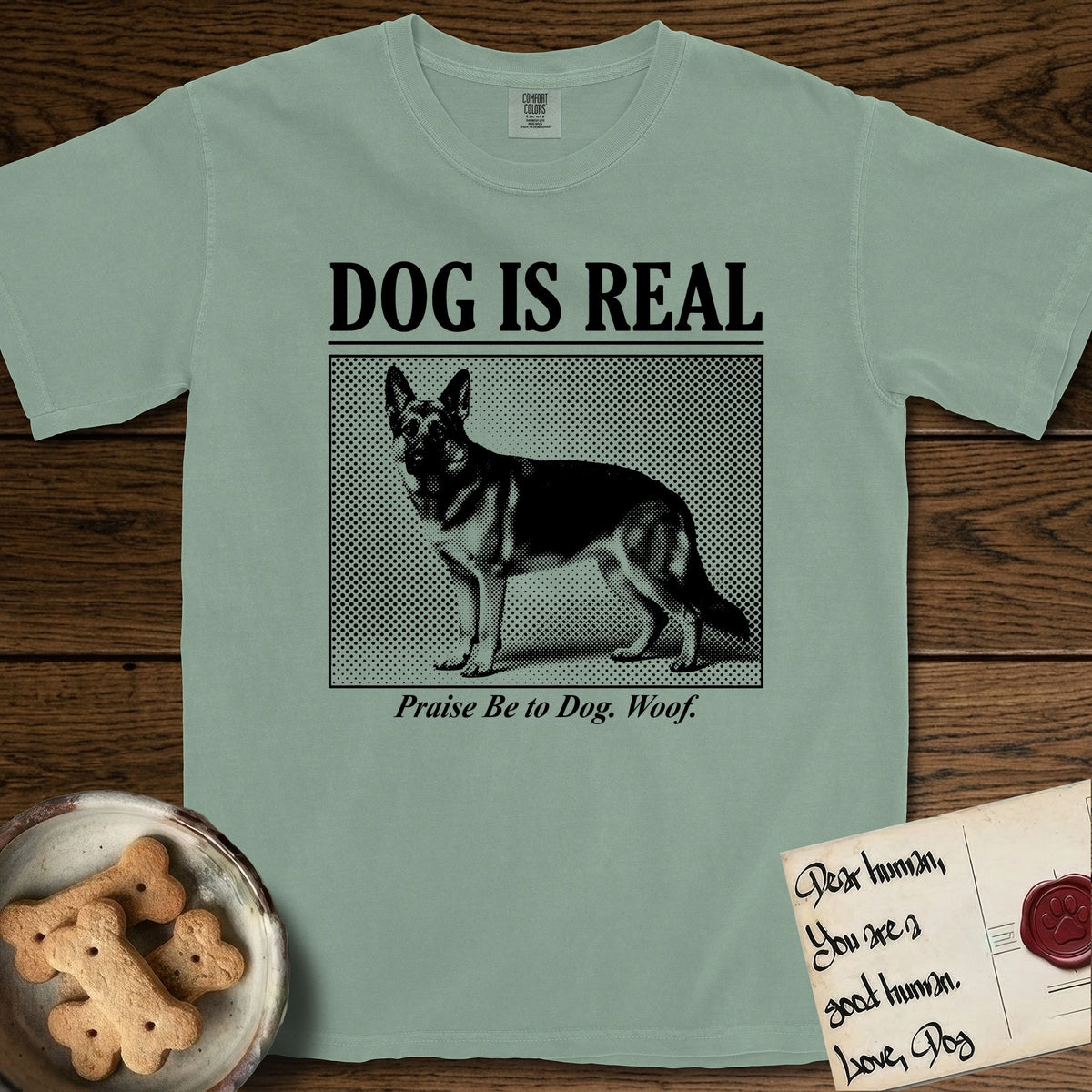Dog is Real German Shepherd T-Shirt flat lay in Bay, featuring Black halftone newspaper photo of a black and tan German Shepherd with upright ears standing in profile with head turned to the camera, under the headline DOG IS REAL, with the caption Praise Be to Dog. Woof..