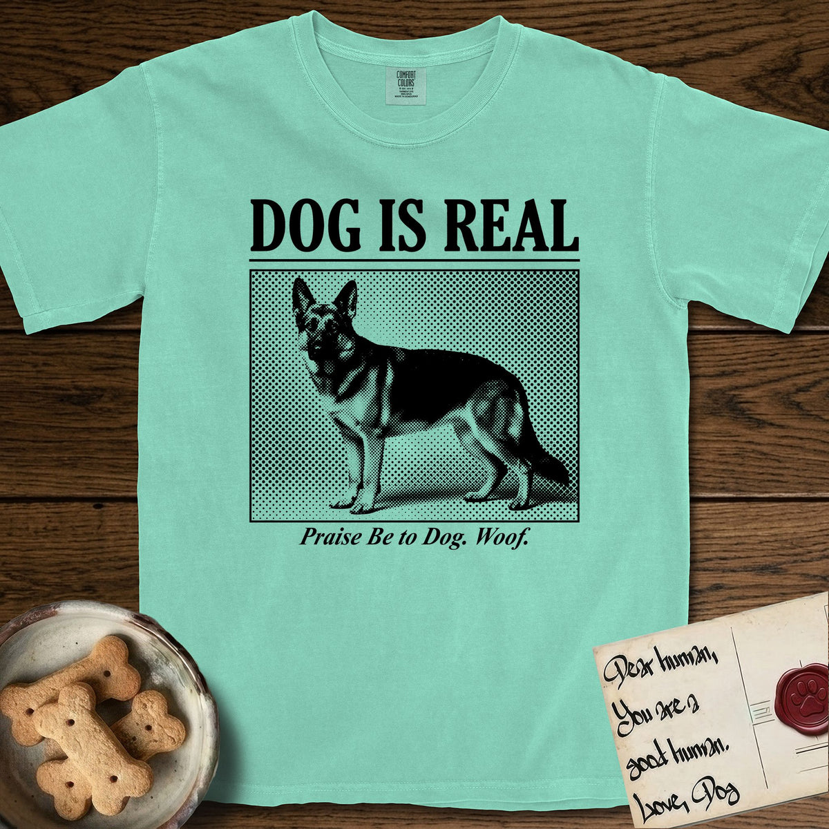 Dog is Real German Shepherd T-Shirt flat lay in Island Reef, featuring Black halftone newspaper photo of a black and tan German Shepherd with upright ears standing in profile with head turned to the camera, under the headline DOG IS REAL, with the caption Praise Be to Dog. Woof..