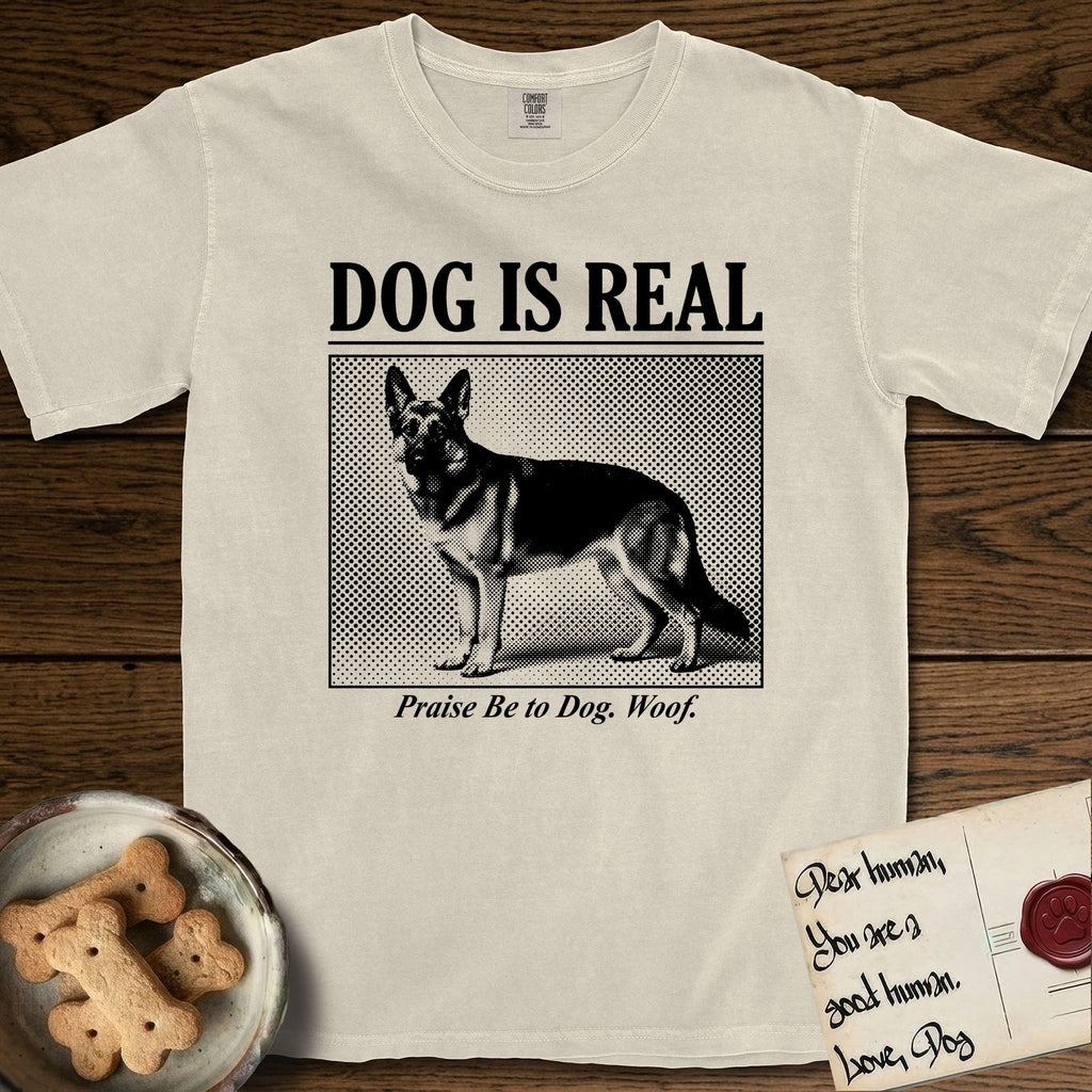 Dog is Real German Shepherd T-Shirt flat lay in Ivory, featuring Black halftone newspaper photo of a black and tan German Shepherd with upright ears standing in profile with head turned to the camera, under the headline DOG IS REAL, with the caption Praise Be to Dog. Woof..
