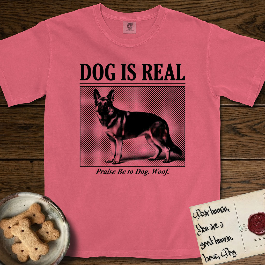 Dog is Real German Shepherd T-Shirt flat lay in Watermelon, featuring Black halftone newspaper photo of a black and tan German Shepherd with upright ears standing in profile with head turned to the camera, under the headline DOG IS REAL, with the caption Praise Be to Dog. Woof..