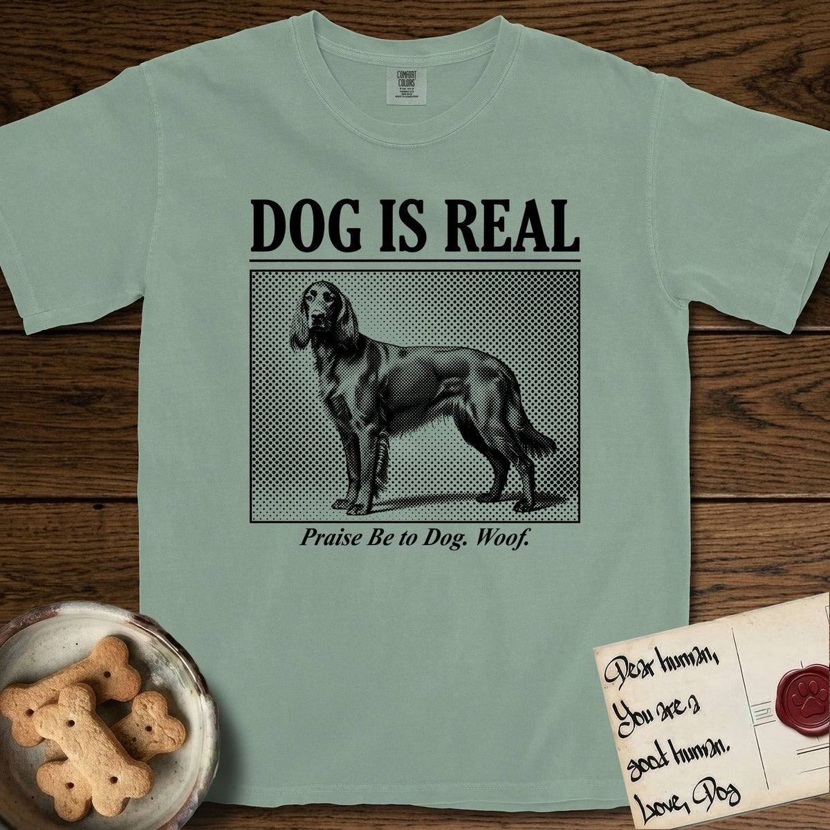 Dog is Real Irish Setter T-Shirt flat lay in Bay, featuring Black halftone newspaper photo of a feathered Irish Setter standing in profile with head turned to the camera, under the headline DOG IS REAL, with the caption Praise Be to Dog. Woof..