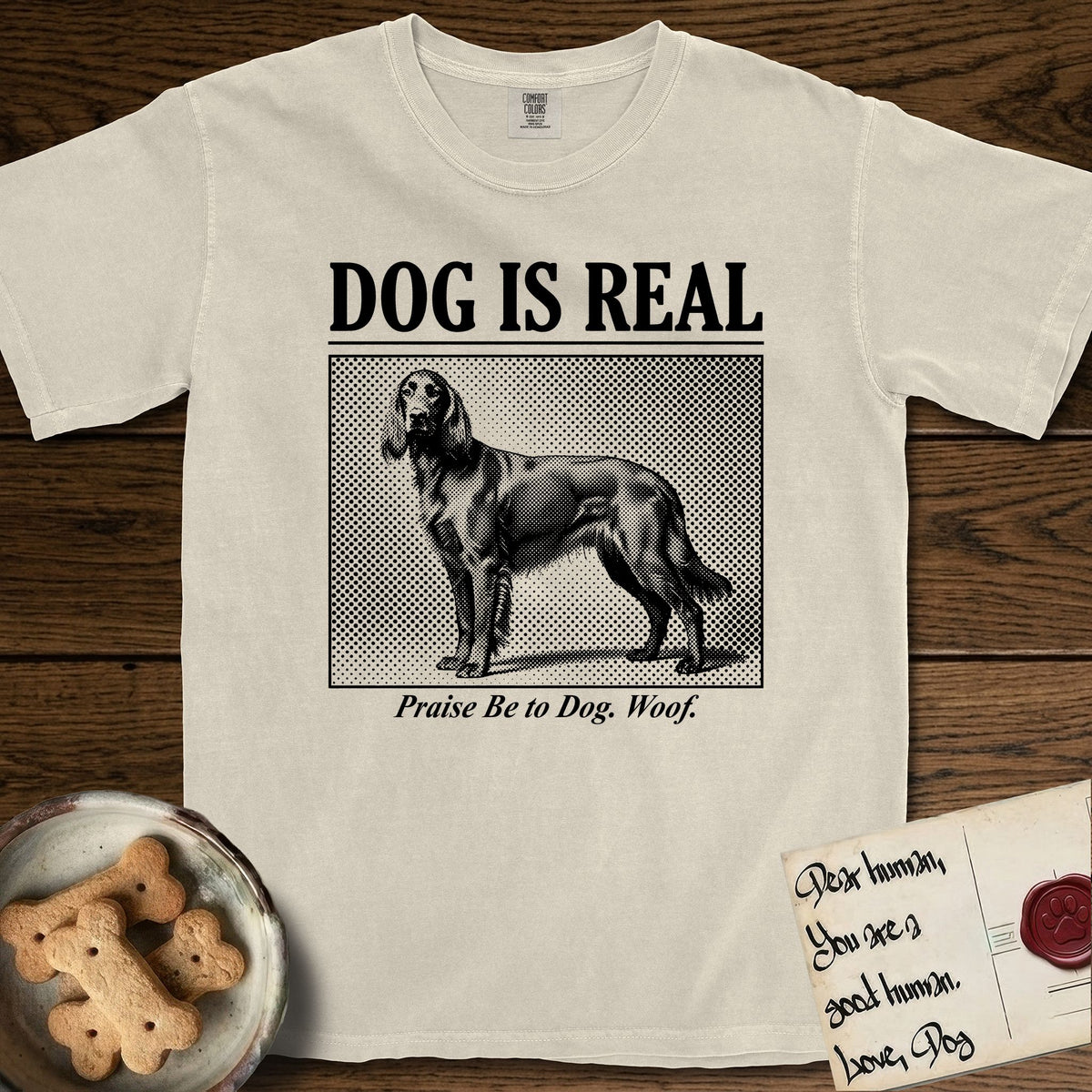 Dog is Real Irish Setter T-Shirt flat lay in Ivory, featuring Black halftone newspaper photo of a feathered Irish Setter standing in profile with head turned to the camera, under the headline DOG IS REAL, with the caption Praise Be to Dog. Woof..