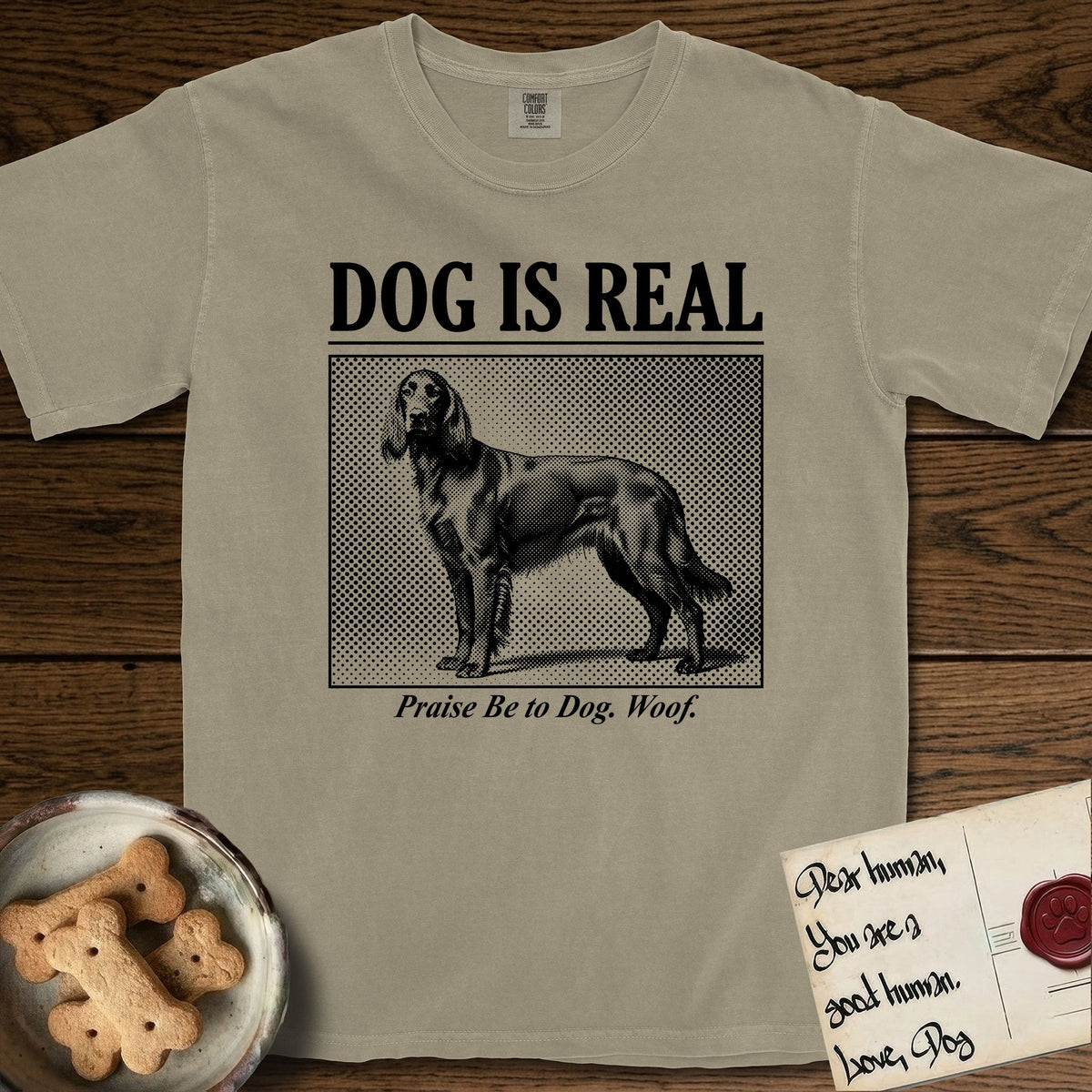 Dog is Real Irish Setter T-Shirt flat lay in Khaki, featuring Black halftone newspaper photo of a feathered Irish Setter standing in profile with head turned to the camera, under the headline DOG IS REAL, with the caption Praise Be to Dog. Woof..