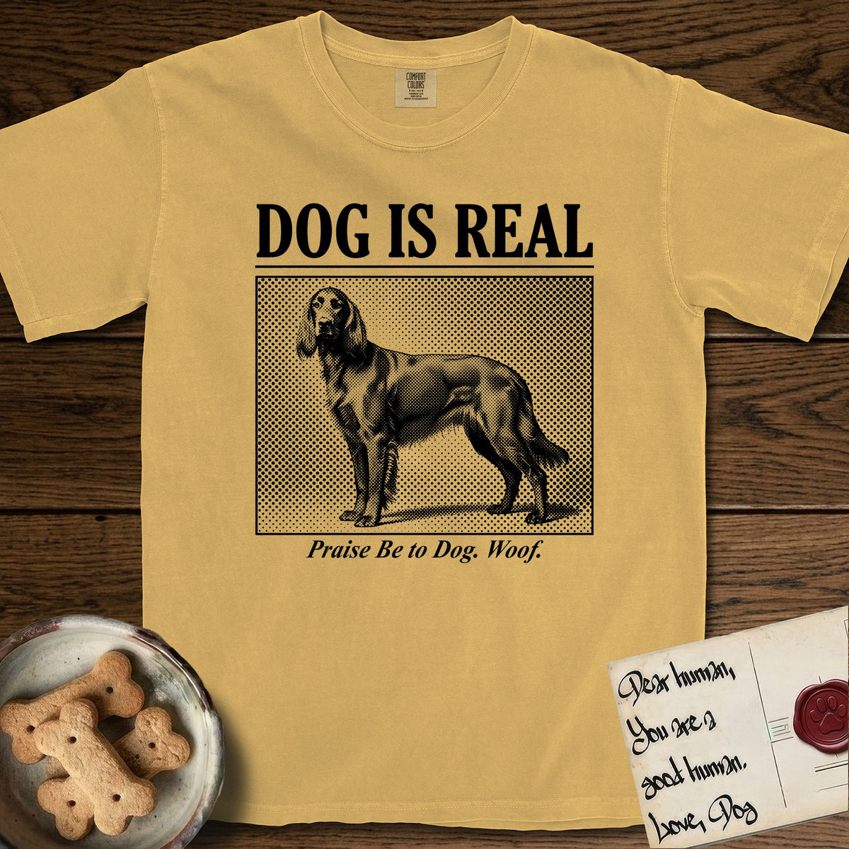 Dog is Real Irish Setter T-Shirt flat lay in Mustard, featuring Black halftone newspaper photo of a feathered Irish Setter standing in profile with head turned to the camera, under the headline DOG IS REAL, with the caption Praise Be to Dog. Woof..