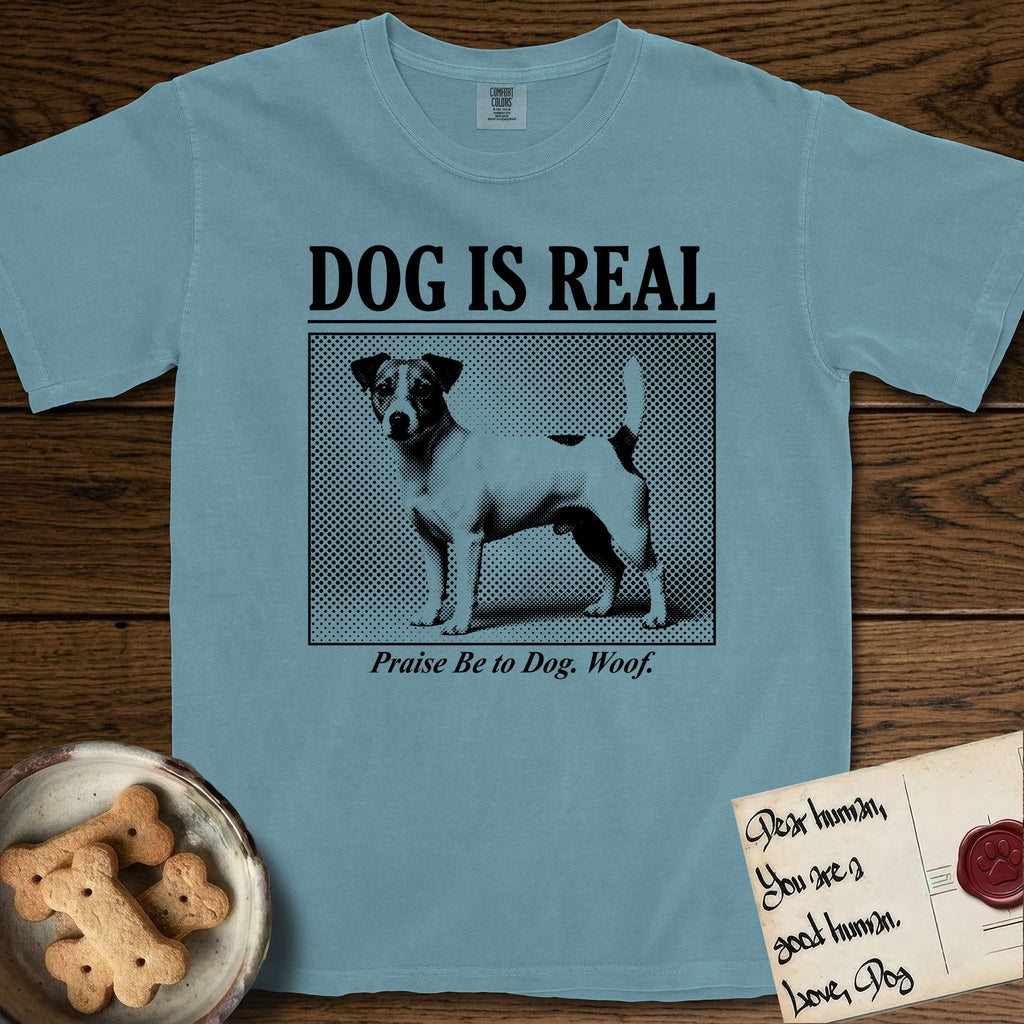 Dog is Real Jack Russell T-Shirt flat lay in Ice Blue, featuring Black halftone newspaper photo of a mostly white Jack Russell with dark ears and an upright tail standing in profile with head turned to the camera, under the headline DOG IS REAL, with the caption Praise Be to Dog. Woof..