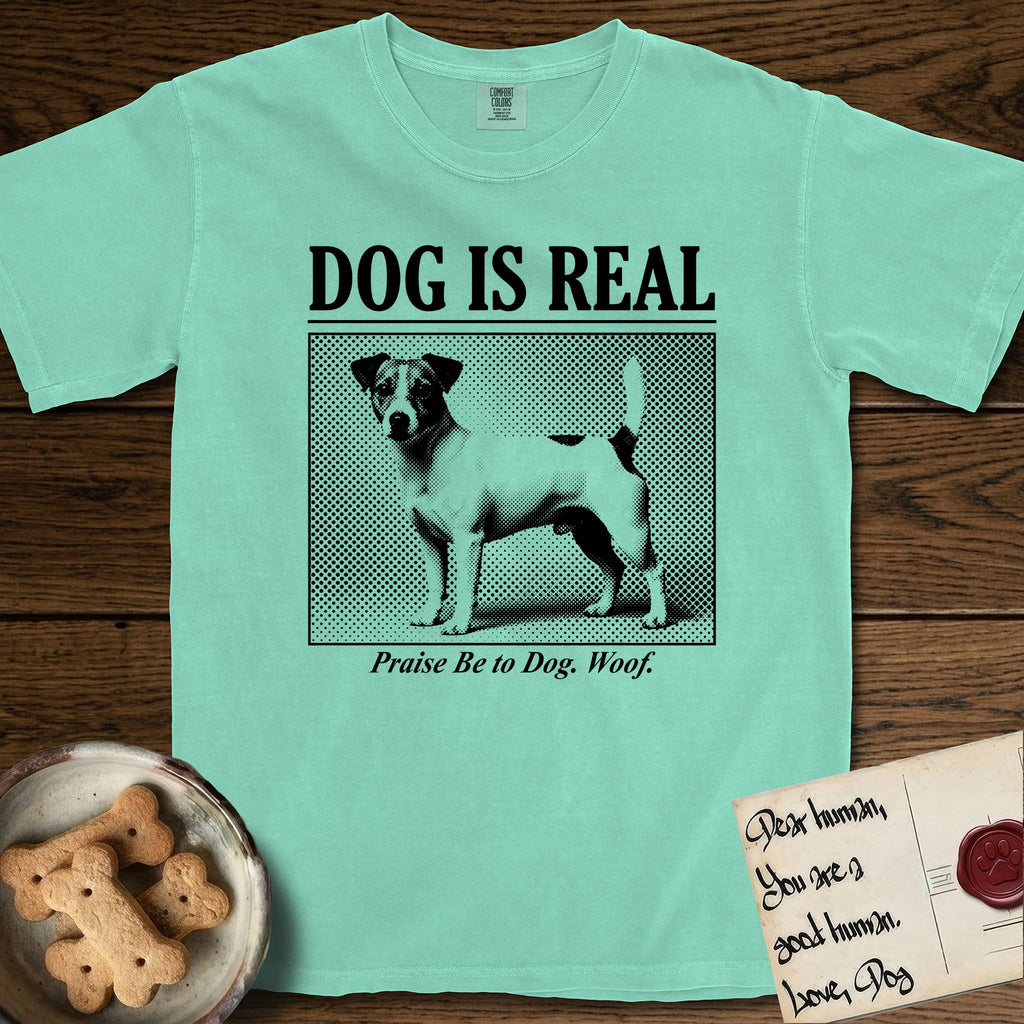 Dog is Real Jack Russell T-Shirt flat lay in Island Reef, featuring Black halftone newspaper photo of a mostly white Jack Russell with dark ears and an upright tail standing in profile with head turned to the camera, under the headline DOG IS REAL, with the caption Praise Be to Dog. Woof..