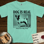 Dog is Real Jack Russell T-Shirt flat lay in Island Reef, featuring Black halftone newspaper photo of a mostly white Jack Russell with dark ears and an upright tail standing in profile with head turned to the camera, under the headline DOG IS REAL, with the caption Praise Be to Dog. Woof..