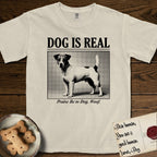 Dog is Real Jack Russell T-Shirt flat lay in Ivory, featuring Black halftone newspaper photo of a mostly white Jack Russell with dark ears and an upright tail standing in profile with head turned to the camera, under the headline DOG IS REAL, with the caption Praise Be to Dog. Woof..
