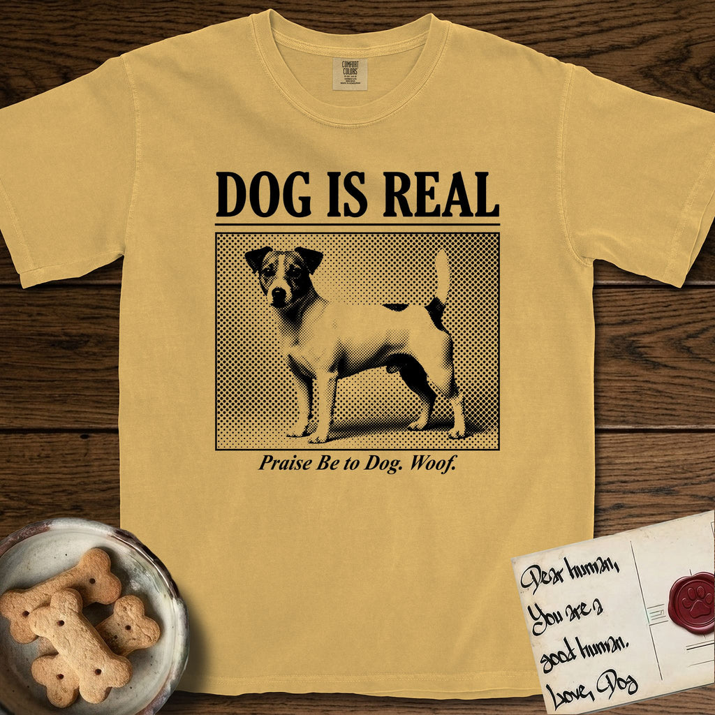 Dog is Real Jack Russell T-Shirt flat lay in Mustard, featuring Black halftone newspaper photo of a mostly white Jack Russell with dark ears and an upright tail standing in profile with head turned to the camera, under the headline DOG IS REAL, with the caption Praise Be to Dog. Woof..