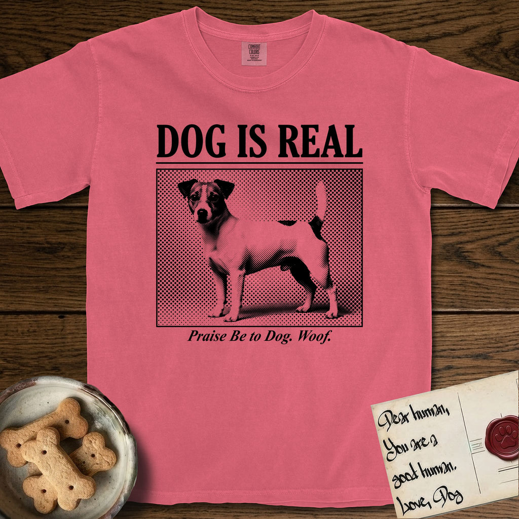 Dog is Real Jack Russell T-Shirt flat lay in Watermelon, featuring Black halftone newspaper photo of a mostly white Jack Russell with dark ears and an upright tail standing in profile with head turned to the camera, under the headline DOG IS REAL, with the caption Praise Be to Dog. Woof..