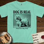 Dog is Real Maltese T-Shirt flat lay in Island Reef, featuring Black halftone newspaper photo of a long-coated white Maltese standing in profile with head turned to the camera, under the headline DOG IS REAL, with the caption Praise Be to Dog. Woof..