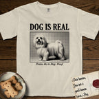 Dog is Real Maltese T-Shirt flat lay in Ivory, featuring Black halftone newspaper photo of a long-coated white Maltese standing in profile with head turned to the camera, under the headline DOG IS REAL, with the caption Praise Be to Dog. Woof..