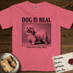 Dog is Real Maltese T-Shirt flat lay in Watermelon, featuring Black halftone newspaper photo of a long-coated white Maltese standing in profile with head turned to the camera, under the headline DOG IS REAL, with the caption Praise Be to Dog. Woof..
