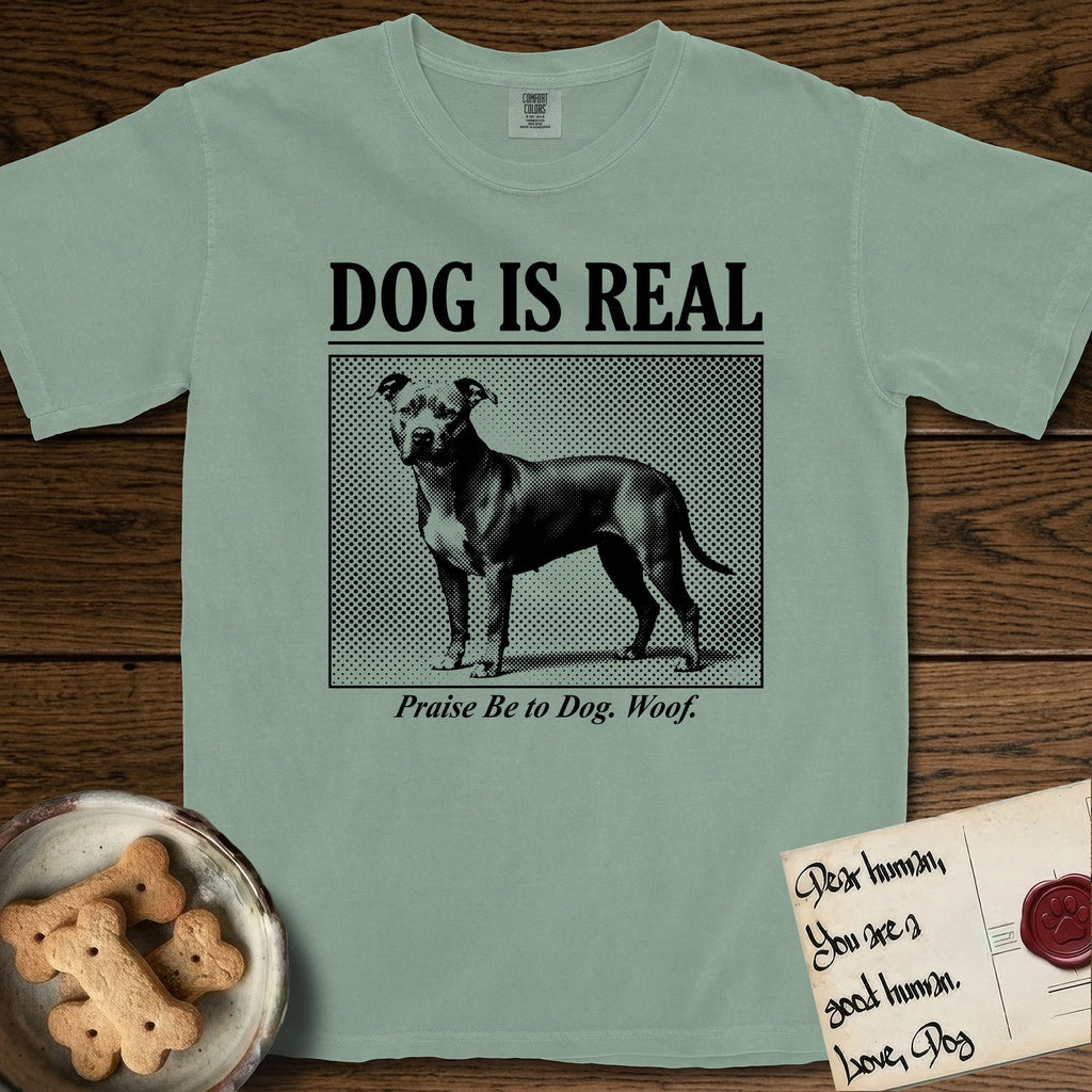 Dog is Real Pitbull T-Shirt flat lay in Bay, featuring Black halftone newspaper photo of a broad-chested Pitbull standing in profile with head turned to the camera, under the headline DOG IS REAL, with the caption Praise Be to Dog. Woof..