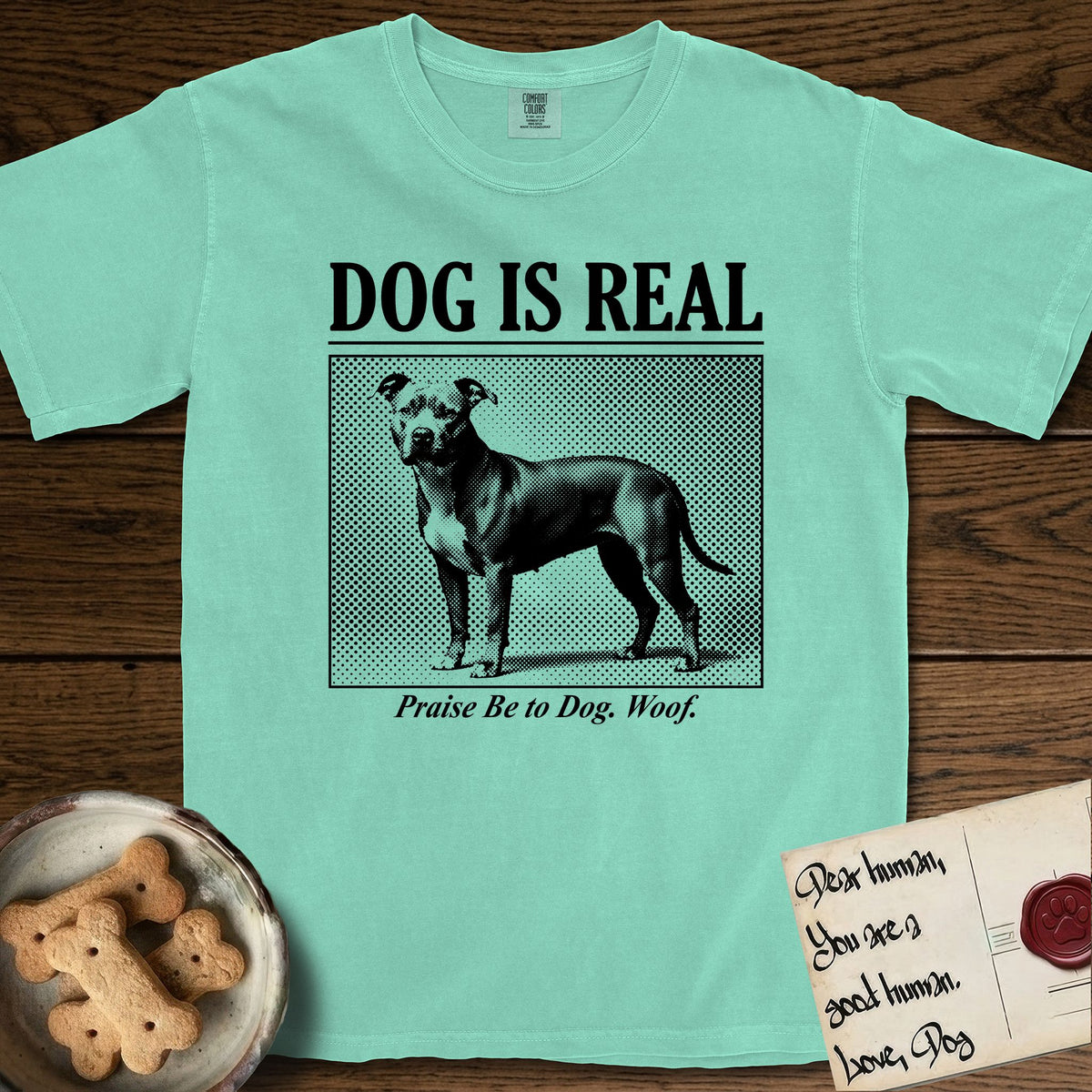 Dog is Real Pitbull T-Shirt flat lay in Island Reef, featuring Black halftone newspaper photo of a broad-chested Pitbull standing in profile with head turned to the camera, under the headline DOG IS REAL, with the caption Praise Be to Dog. Woof..