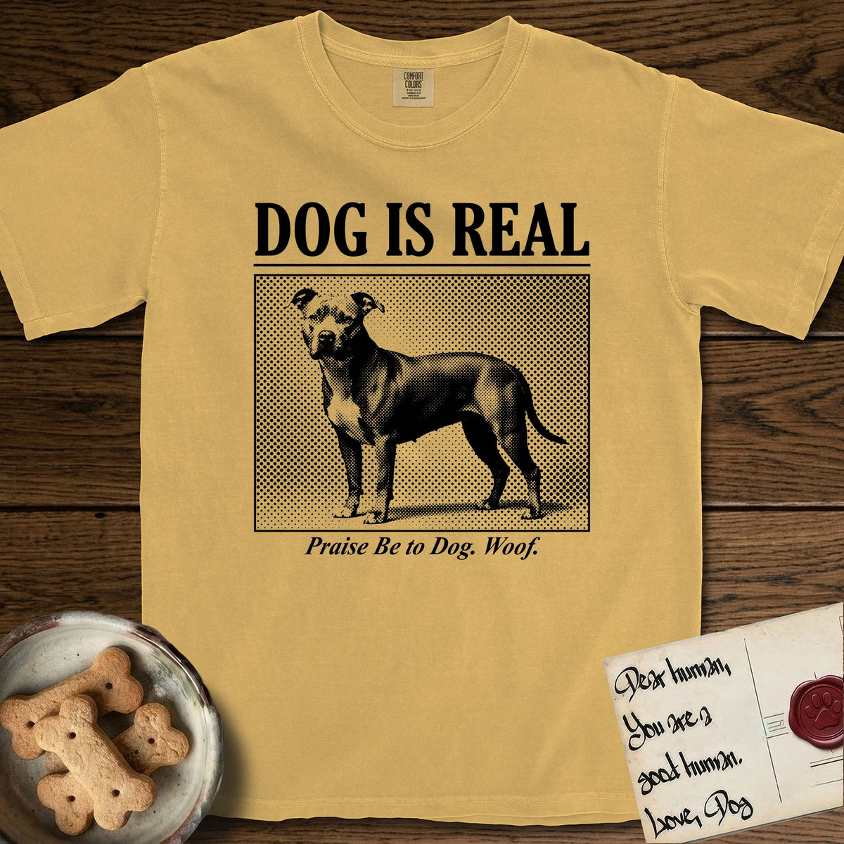 Dog is Real Pitbull T-Shirt flat lay in Mustard, featuring Black halftone newspaper photo of a broad-chested Pitbull standing in profile with head turned to the camera, under the headline DOG IS REAL, with the caption Praise Be to Dog. Woof..